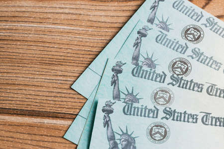 A group of IRS refund stimulus payment checks laying on a wooden deskの写真素材