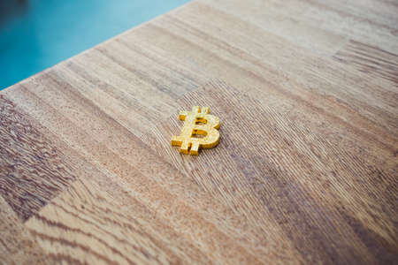 One single golden bitcoin cryptocurrency symbol laying on a wooden desk