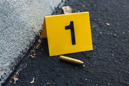 One yellow crime scene evidence marker on the street after a gun shooting brass bullet shell casing...