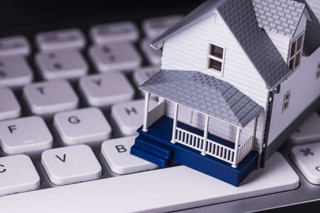 Miniature white house sitting on a white computer keyboard real estate vacation rental homeの写真素材