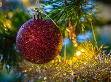 A red Christmas ball hung on a tree with other Christmas decorations.の写真素材