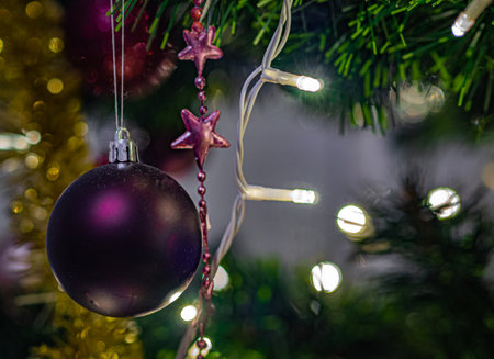 A purple Christmas ball hangs on a tree with lights around it and a bokeh background.の写真素材