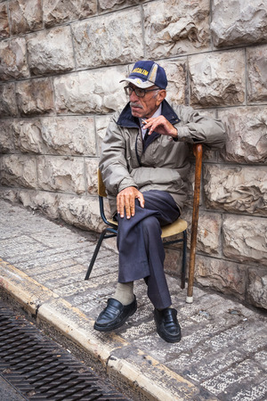 JERUSALEM / ISRAEL - NOVEMBER 19, 2016: Old man sitting and smoking in a chair on the sidewalk in the old city of Jerusalem, Israel.のeditorial素材