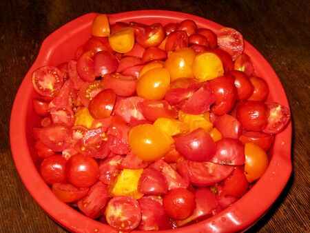A red bowl with juicy chopped tomatoes close-up, stands on the table. Chopped tomatoes in a bowl. Bio tomatoes, for preparing a homemade sauce, ketchup.の写真素材