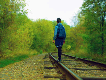 A young man stands on the railway tracks and looks into the distance. Back view. Active rest on the travel on foot. Wild nature.の写真素材