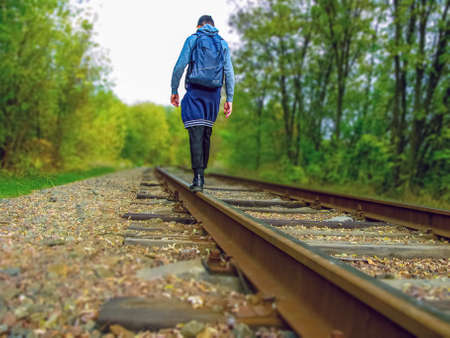 A young man walks along the railroad tracks. Back view. Active recreation on foot. Wildlife.の写真素材