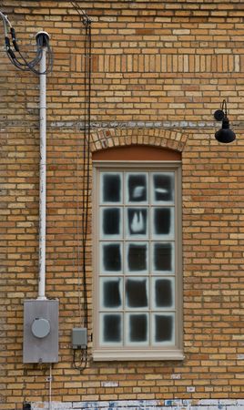 Window in a yellow brick wall with lights on wall and meter boxの写真素材