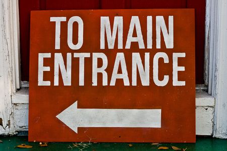 Red sign with white writing arrow pointing to main entrance