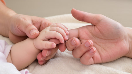 Close-up of adult and baby hands gently holding each other, highlighting warmth and affection, with soft textures and a calming atmosphere, representing family loveの素材