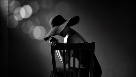Stylish female figure in a large hat sits on a chair, with blurred lights in the background, evoking a sense of elegance and artistic expressionの素材