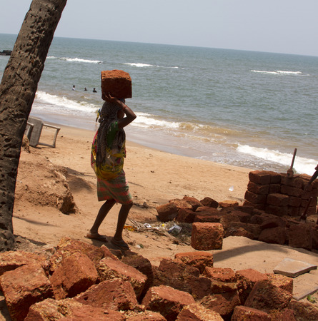 The Indian woman in a sari stones for building on the head on a beach. India Goa.の写真素材