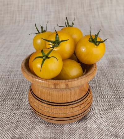 Fresh yellow cherry tomatoes in a wooden rustic jar.の写真素材