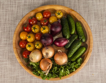 Fresh red and yellow cherry tomatoes and cucumbers, onions on a wooden tray in a rustic style. Good ingredients for the salad, cucumbers, tomatoes, onions and green salad mix.の写真素材