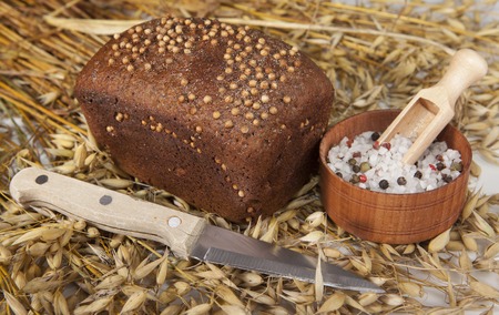 Loaf of homemade bread with black mustard seeds on a table with spikelets of rye and oat sand salt shaker salt and knife.の写真素材