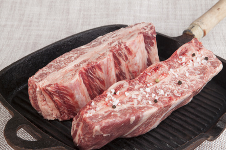 Close-up of two pieces of fresh marbled beef with sea salt and black pepper, on a cast-iron grill pan.の写真素材