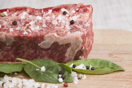 Close-up piece of fresh marbled beef, chili pepper, parsley, onion, garlic, ribs lie on a wooden tray.の写真素材
