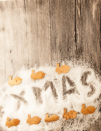 Christmas card with the inscription xmas with christmas small rabbits from birch bark  in the snow on a wooden background.の写真素材