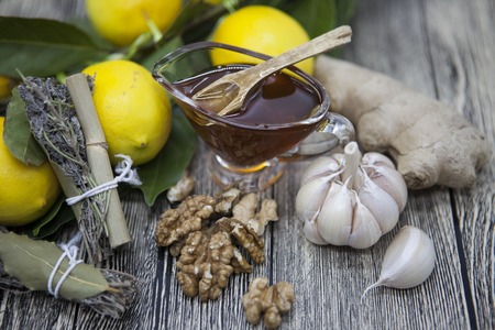 The composition of glass vase with floral honey and wooden spoon with lemon provencal herbs walnuts, garlic  and ginger on a wooden background.の写真素材