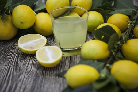 Fresh juicy lemons and a glass of homemade lemonade on a wooden background.の写真素材