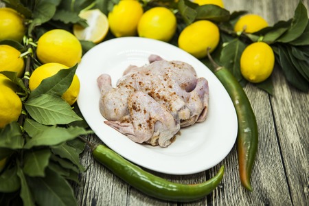 Raw fresh chicken on porcelain plate with lemon and chilli  on the wooden background.の写真素材