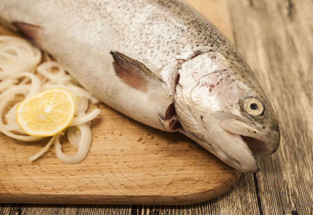 Fresh Norwegian rainbow trout with lemon and onions on a wooden background.の写真素材