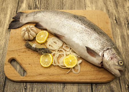 Fresh Norwegian rainbow trout with lemon and onions on a wooden background.の写真素材