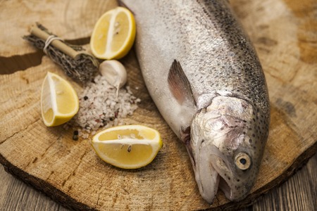 Fresh Norwegian rainbow trout with lemon and onions on a wooden background.の写真素材