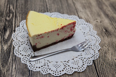 Fresh tasty sweet piece of cheese cake on a white napkin and a dessert fork on a wooden background.の写真素材
