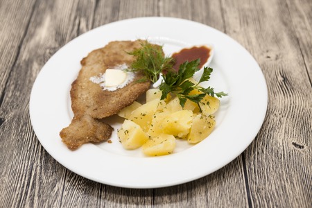 Petite Wiener schnitzel with boiled potatoes and ketchup. Served on a white porcelain plate on a...