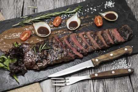 Delicious juicy hot roast beef cut into delicious pieces of meat and vegetables. Served on a black stone plate with a fork and knife and pepperの写真素材