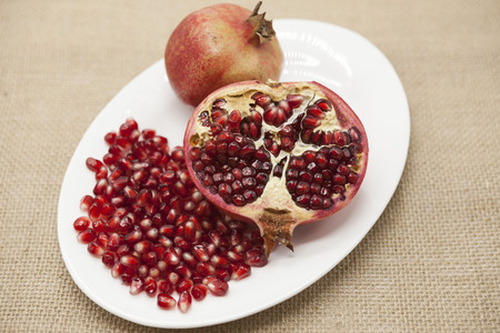 Pomegranates have broken into pieces with red berries on a porcelain plate on a textile backgroundの写真素材