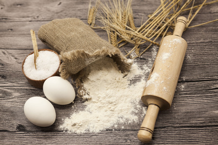 Wheat flour in a canvas bag, with spikelets of rye, a large salt shaker wood, raw eggs, a wooden rolling pin: set for making homemade bread dough on a beautiful dark wooden background.の写真素材