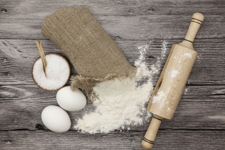 Wheat flour in a canvas bag, a large salt shaker wood, raw eggs, a wooden rolling pin: set for...