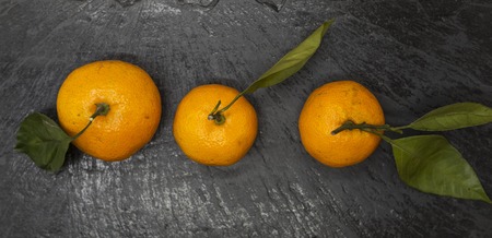 Fresh juicy tasty Sicilian tangerines with a foliage branch on a stone backgroundの写真素材