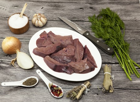Pieces of fresh raw beef liver, onion, garlic, spices, dill, parsley, salt, knife, olive oil on...