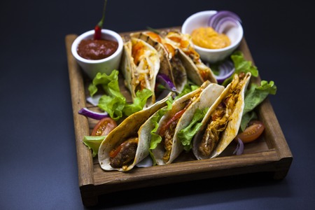 Mexican Tortilla with meat, beef and stewed vegetables and spicy sauce on a wooden trayの写真素材