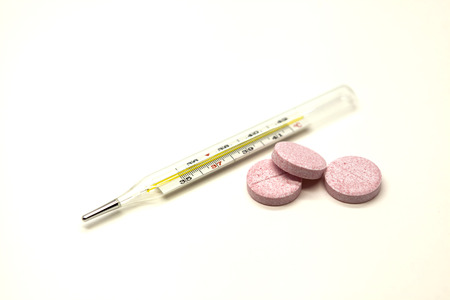 Old mercury medical thermometer with pills closeup on white background.