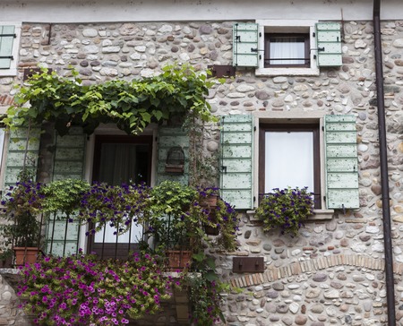 Old window with open shutters with flowers on the window sill on the stone wall. Italian Village.の写真素材