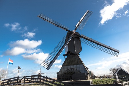 Old windmill with the Netherlands flag. White clouds on a blue sky, the wind is blowingの写真素材