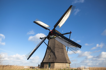 Old windmill stands on the banks of the canal, and water pumps. White clouds on a blue sky, the wind...
