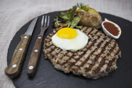 Big, juicy, delicious beefsteak with a fried egg and baked potatoes on a stone plateの写真素材