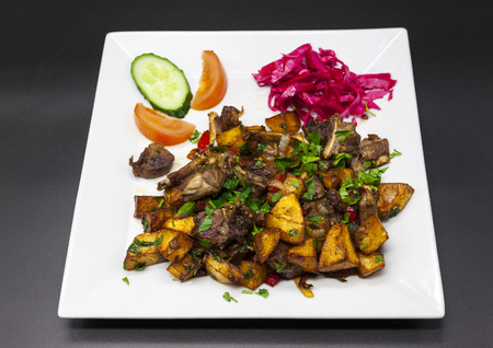 Pork ribs with fried potatoes on the platter on a black background. Roast pork with potatoes and red cabbage with cucumber and tomato on the plate.の写真素材