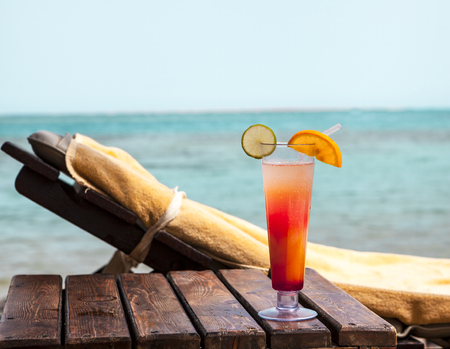 A glass goblet with a cocktail on a deckchair on the beachの写真素材