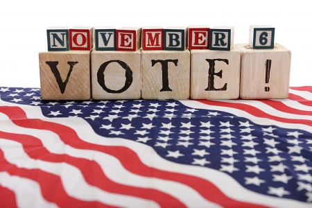 Large, rustic alphabet blocks arranged to spell,  VOTE   with smaller, red, white and blue alphabet blocks that spell out  November 6    All set upon stars and stripes   の写真素材