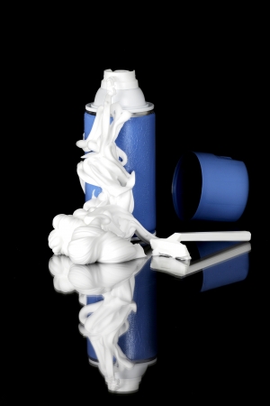 White foam spilling out of a blue can of shaving cream with its reflection.  On a black background.の写真素材
