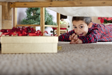 A young elementary boy delighted at seeing a boxed gift under his parents' bed.  の写真素材