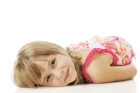 Closeup of a pretty young elementary girl happily resting on her belly.  On a white background.の写真素材