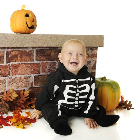 An adorable baby boy  skeleton  sitting against a brick wall with pumpkins and colorful leaves nearby   On a white background の写真素材