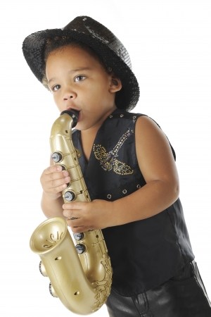 An adorable preschooler playing a toy saxophone in a sparkly black fedora and balck leather vest and pants.  On a white background.の写真素材