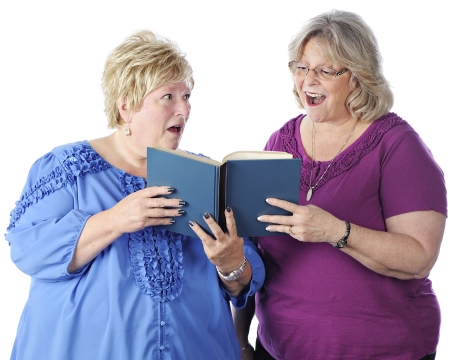 Two senior women singing from the same book.  One looks at the music happily while the other scowls as she looks at her.  On a white background.の写真素材